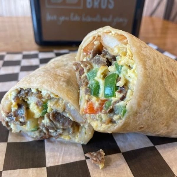 A Biscuit Bros breakfast burrito, cut in half, revealing eggs, meat, and colorful vegetables.