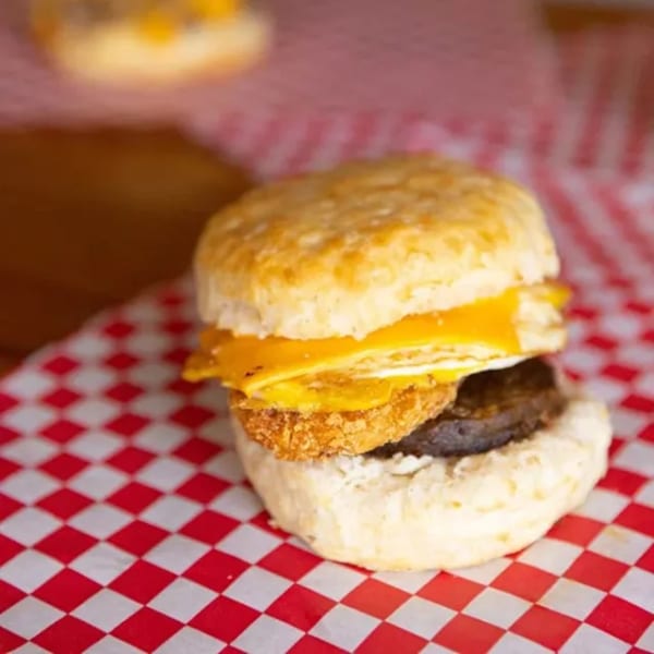 Biscuit Bros' breakfast sandwich with egg, cheese, and sausage on red and white checkered paper.