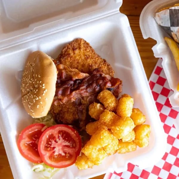Biscuit Bros' fried chicken, bacon, tater tots, tomato, and bun in a takeout container.