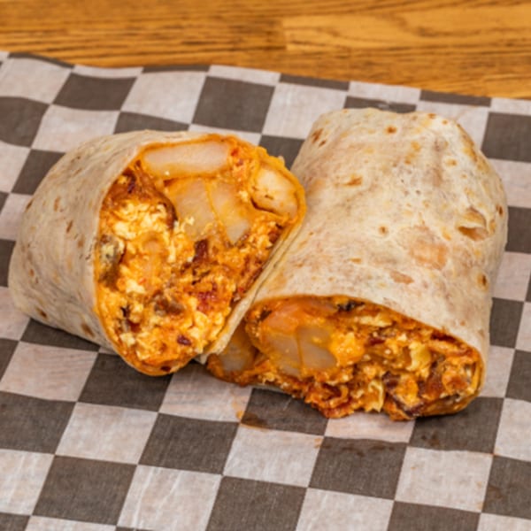 A breakfast burrito from Biscuit Bros, cut in half, revealing eggs, potatoes, and cheese.
