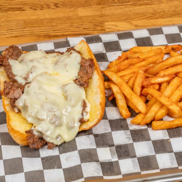 A Biscuit Bros cheesesteak sandwich with melted cheese and a side of golden fries on checkered paper.
