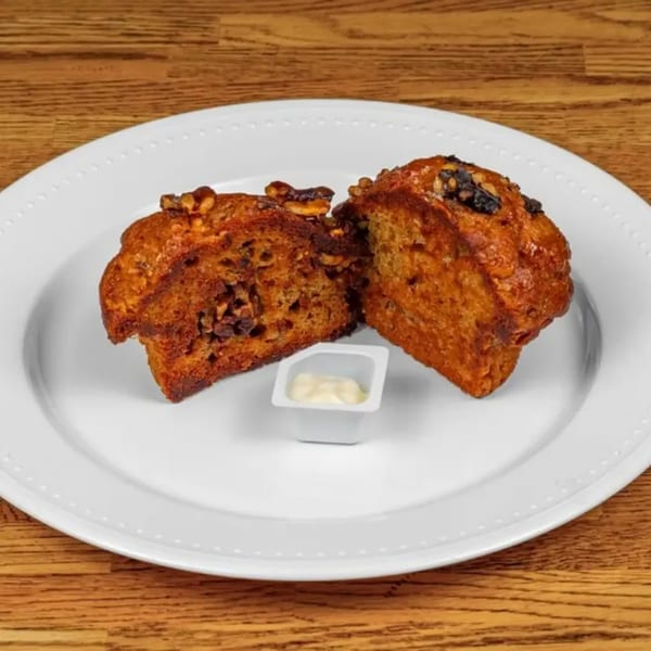 Two halves of a golden-brown muffin with nuts and chocolate chips, served with butter on a white plate.