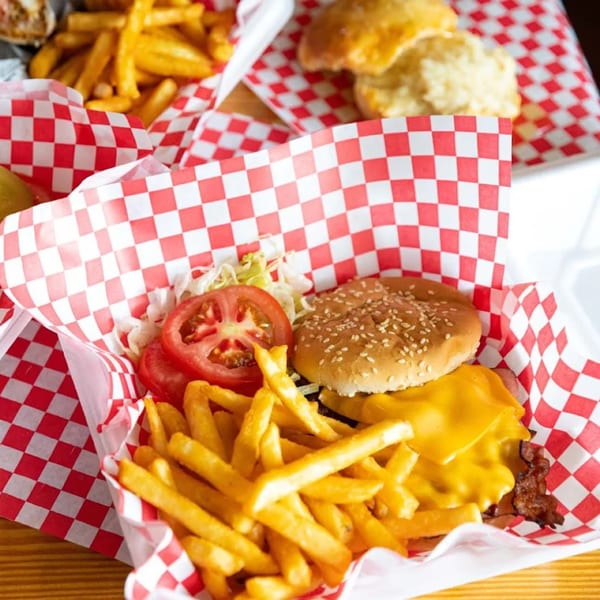 A Biscuit Bros burger with cheese, bacon, lettuce, tomato, and fries in a red checkered basket.